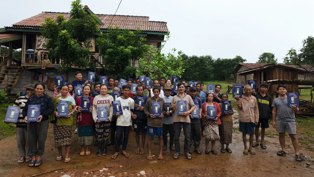ຄົນໃນຊຸມຊົນຖືກ່ອງໄຟ SOLARO HOME ຖ່າຍຮູບຮ່ວມກັນຢູ່ໜ້າເຮືອນໄມ້
